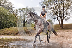 Girl riding gray horse down the calm river water