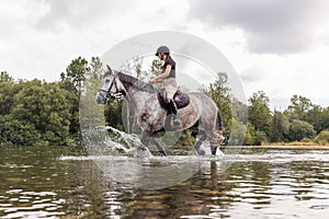 Girl riding gray horse down the calm river water