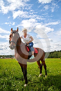 Girl riding on a horse on a green field and a blue sky with white clouds on the background