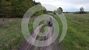 A girl riding a moto scooter or motorcycle along a dirt road between field and forest.Aerial, drone footage.