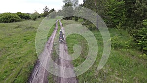 A girl riding a moto scooter or motorcycle along a dirt road between field and forest.Aerial, drone footage.