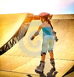 Girl riding on roller skates in skatepark. Backlit on background.