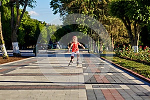 Girl riding on roller skates in skatepark summer outdoor. Child in a red suit for the rollers