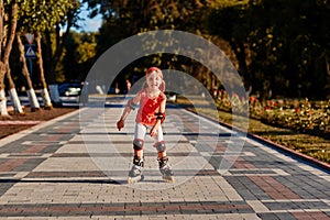 Girl riding on roller skates in skatepark summer outdoor. Child in a red suit for the rollers