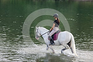 Girl riding a snow white horse down the calm river water