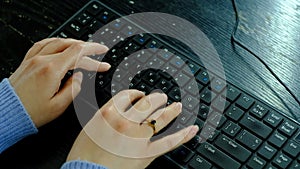 Girl with a ring on her finger typing text on a black keyboard.