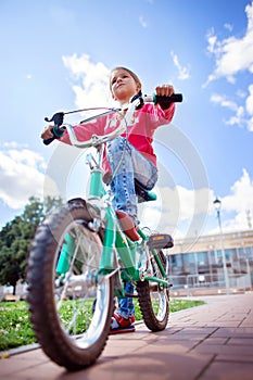 A girl in ripped jeans rides a bicycle in the park. Bottom view