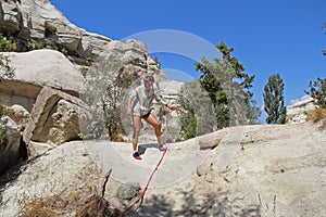 The girl rises by the steep hill by means of rope. Rock formation at the end of the Zemi valley between Gereme and Uchisar, Cappad