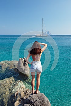 Girl on the rock looking to the yacht on sea