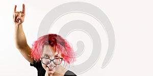 A girl rocker with red hair and glasses squinting one eye shows a hand gesture Heavy Metal HM on a white background