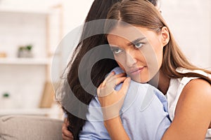 Girl Rolling Eyes Embracing Crying Friend Sitting On Sofa