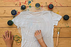 The girl rolls up a white t-shirt for the application of tie dye style.