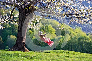 A girl in a romantic image swings on a swing. Beautiful, lush, flowering cherry tree is dotted with flowers. Naturel spring