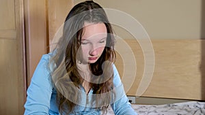 girl in room put head down sit on bed in hands with phone watch video of social network reflection interest in herself