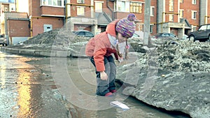 Girl in rubber boots jumping on puddle near wite paper boat