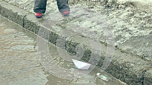 Girl in rubber boots jumping on puddle near wite paper boat