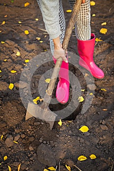 A girl in rubber boots stands in the garden with a shovel and digs. Close-up