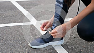 Girl runner tying laces for jogging her shoes on road in a park.