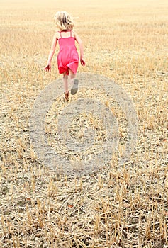 Girl running across a cut corn field