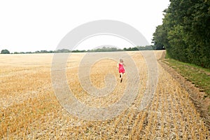 Girl running across a cut corn field