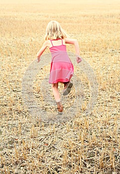 Girl running across a cut corn field