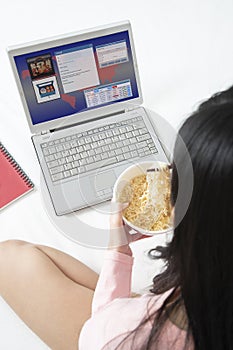 Girl running ebusiness on notebook computer while eating instant