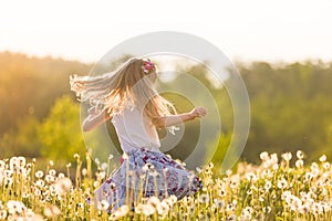 Girl running on the field of dandelions on summer sunset. Beautiful little kid girl  dancing on dandelion meadow with summer