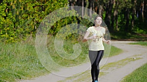 Girl running on forest path in a park and taking breath after jogging. Portrait of tired athlete woman resting, close up