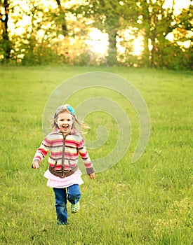 Girl running in green field at sunset