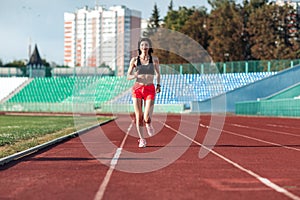 Girl running track on stadium. Real front view of young woman in pink shorts and tank top and pink sneakers. Outdoors, sport