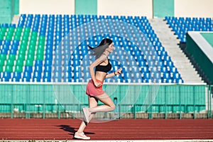 Girl running track on stadium. Real side view of young woman in pink shorts and tank top and pink sneakers. Outdoors, sport