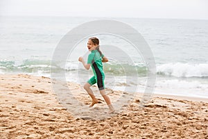 Girl running on tropical beach, having fun, smiling, dressed in protective wetsuit