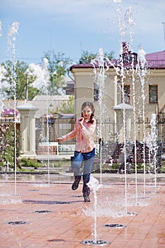 Girl running through the water jets in a fountain.