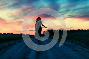 A girl runs along a field road without touching the ground in the evening at sunset a silhouette against the multicolored sky