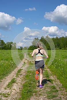 Girl runs along a road that runs through fields under a blue cloudy sky on a summer day.