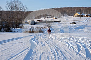 The girl runs away over the frozen lake in the direction of the village on a hill, on a winter sunny day