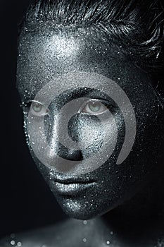 The girl`s beautiful face is painted silver with sequins. shiny metal powder particles sparkle on the model`s face