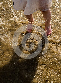 Girl`s feet in the sandy sea water jumping and splashing