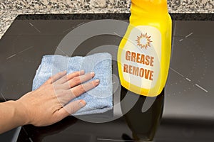 A girl`s hand with a blue microfiber cloth rubs a glass ceramic stove in the kitchen