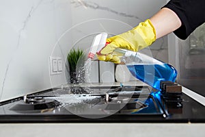 A girl& x27;s hand with a cleaning spray sprays on a built-in gas stove. Modern anti-grease, antistatic cleaning product