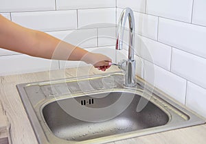 The girl`s hand is holding on to the water tap from which water does not flow in the kitchen. Concept of shutting down the water