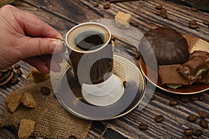 The girl`s hand holds a Cup of coffee over a wooden table with brown sugar, coffee beans and chocolate