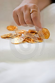 A girl's hand picking up a gold coin from a pile