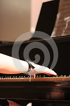Girl's hand playing black grand piano, vertical photo