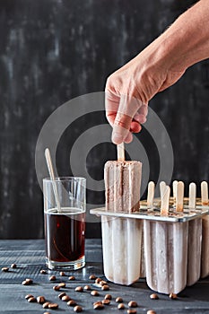 The girl`s hand takes from the mold, homemade natural ice cream on a stick on a black wood table with space for text