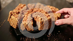 Girl's hand takes a piece of oat cake from black plate on a black table.