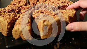 Girl's hand takes a piece of oat cake from black plate on a black table.