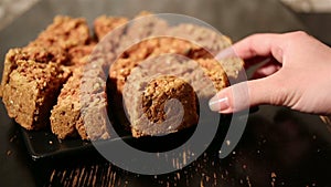 Girl's hand takes a piece of oat cake from black plate on a black table.