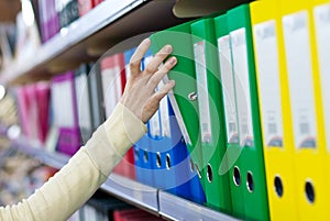 Girl's hand taking big folder from the shelves with office files.