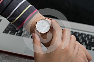 Girl`s hand with wrist watch in front of desk with laptop comput